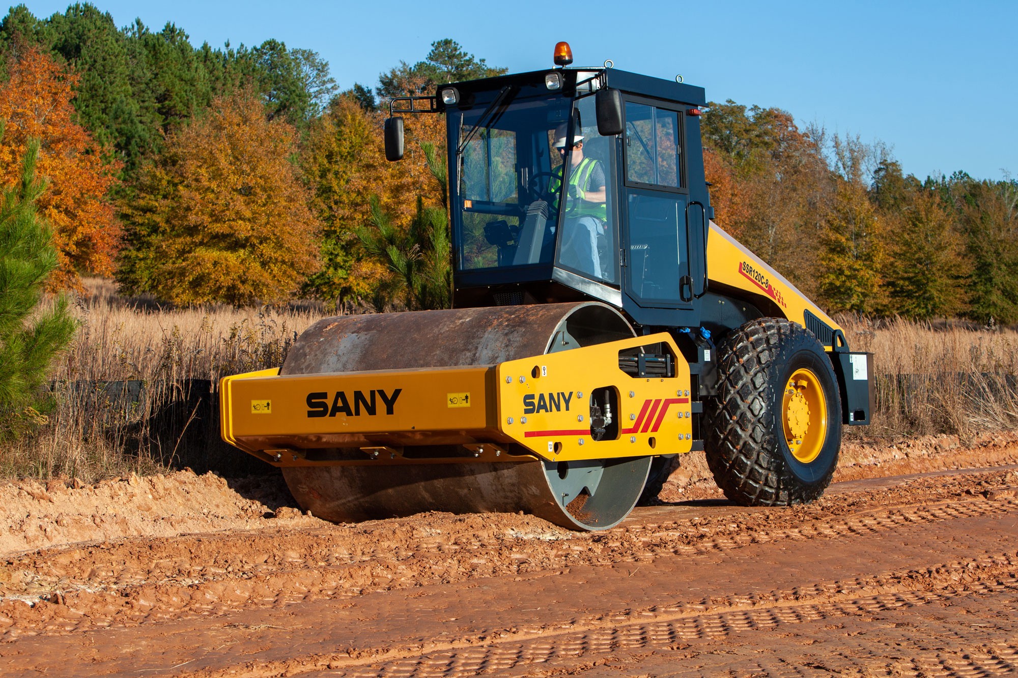 SANY road roller compacting red dirt on a construction site, operated by a worker in hi-vis gear